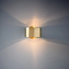 Gold wall-mounted light fixture casting a warm glow on a gray wall.