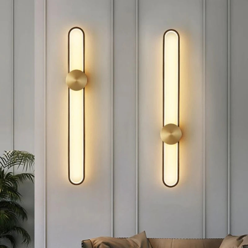 Two modern wall lights on a gray paneled wall with a plant and sofa in the background.