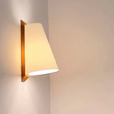 Wall-mounted light fixture with a beige shade on a plain wall.