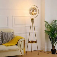 Gold floor lamp with a glass shade in a living room setting. Nordic tripod glass floor lamp with gold finish for a modern living room.