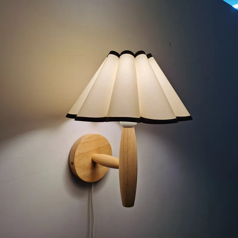 Wall-mounted lamp with a white shade and wooden base on a plain wall.