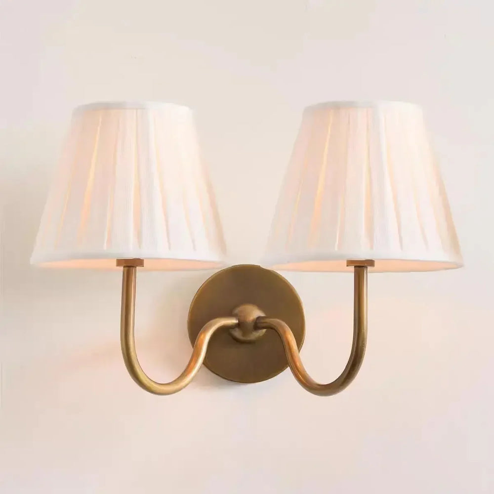 Wall-mounted lamp with two white shades and gold fixture on a light beige wall.