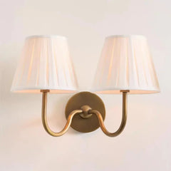 Wall-mounted lamp with two white shades and gold fixture on a light beige wall.