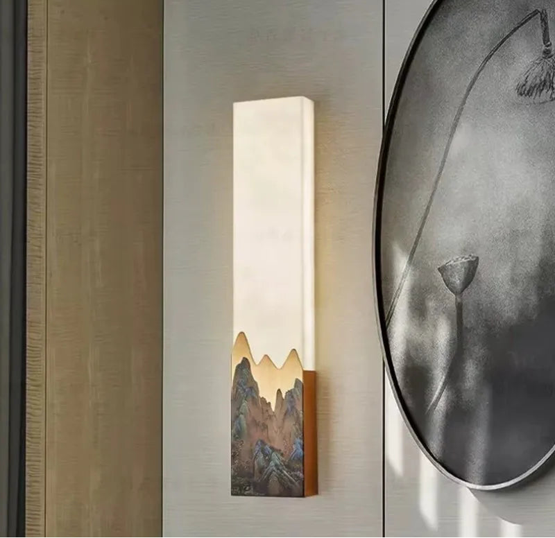Wall-mounted light fixture with mountain design on a neutral wall.