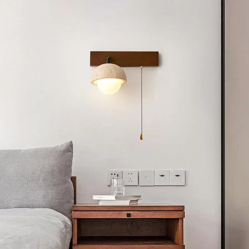 “Travertine stone wall lamp with wood backplate above a bedside table.”