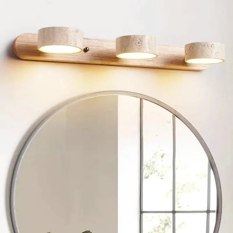 “Travertine and wood vanity wall lamp mounted above a round bathroom mirror.”