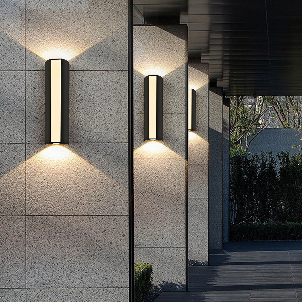 “Black vertical up-and-down LED wall lamp illuminating a stone exterior wall.”