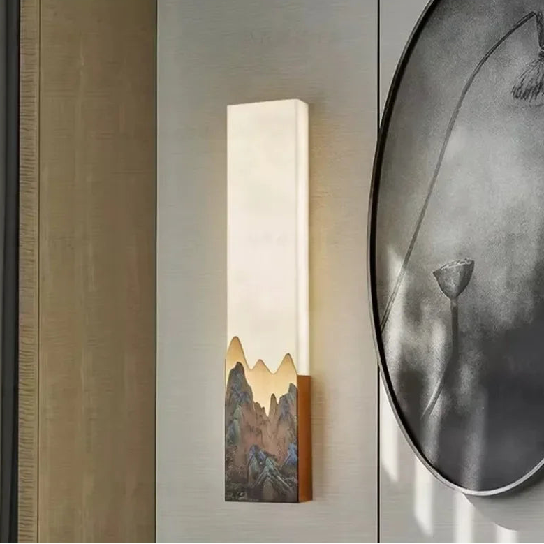 Wall-mounted light fixture with mountain design on a wall next to a round wall art piece.