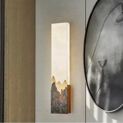 Wall-mounted light fixture with mountain design on a wall next to a round wall art piece.