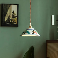 Decorative pendant light with floral design on a green wall with a painting and plant. Vintage artisan hand-painted ceramic ceiling lamp with floral design.