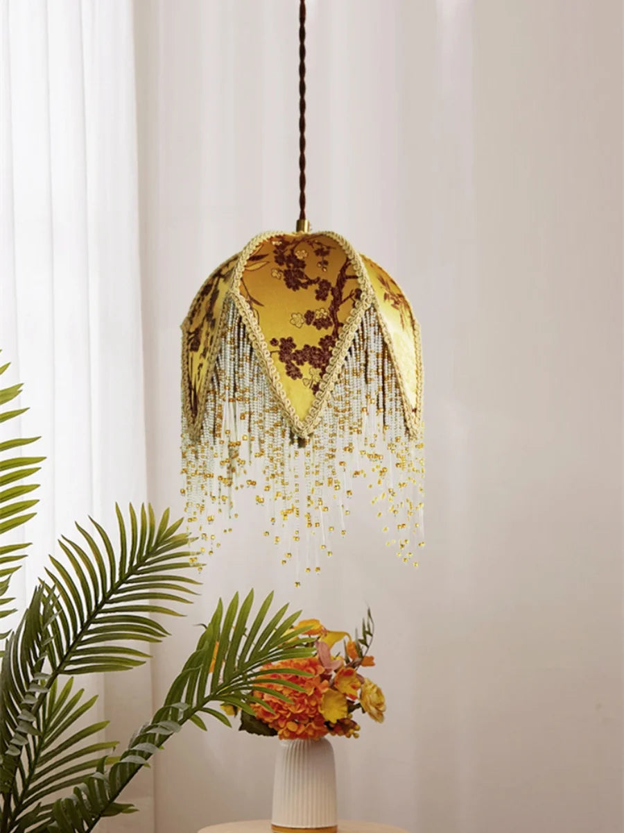 “Artisan fabric pendant lamp with decorative gold or green fringe”