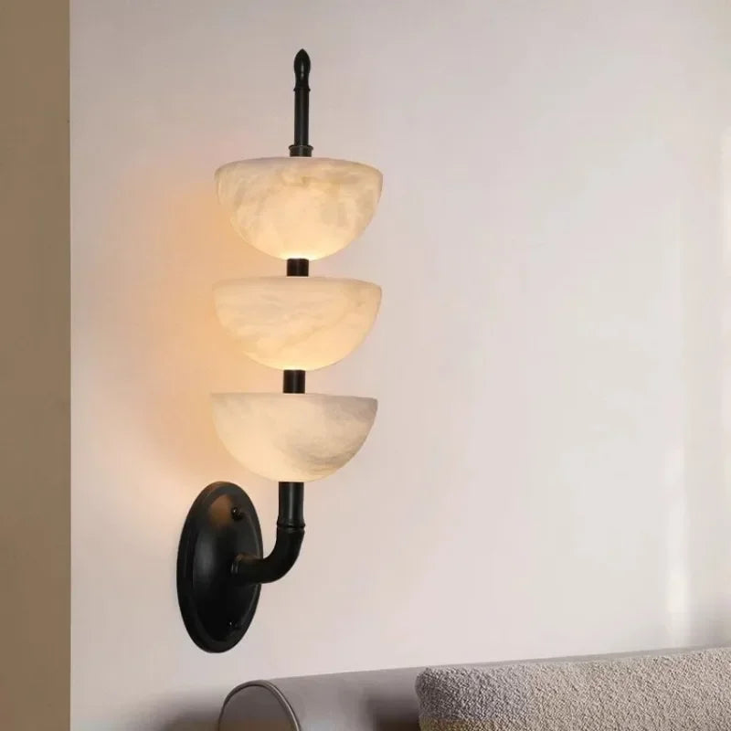 Wall-mounted light fixture with three glass shades on a neutral background