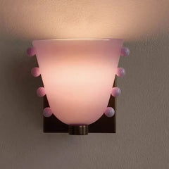 Wall-mounted light fixture with pink glass shade and decorative elements on a neutral background