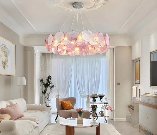 Pink Murano glass discs arranged in a circular chandelier, suspended from a white ceiling with ornate molding.