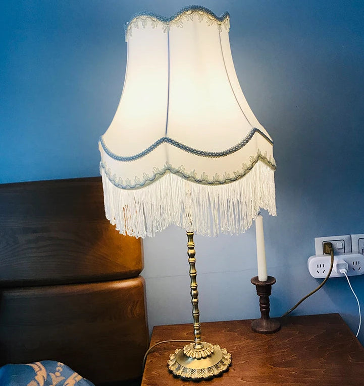 Table lamp with a cream fabric bell lampshade with fringe and blue trim