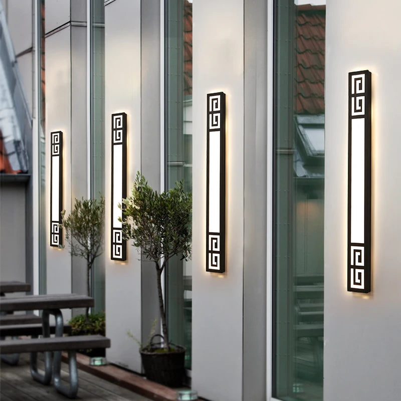 Four modern black geometric LED wall sconces mounted on a building exterior, illuminating a patio area.