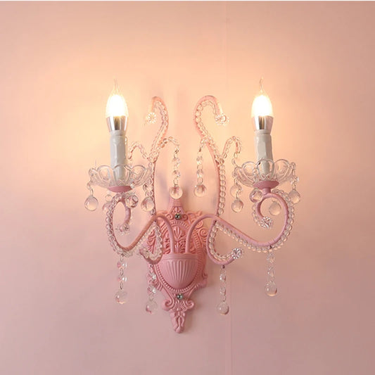 Pink painted metal wall sconce with clear crystal accents and two candle-style lights against a pink wall