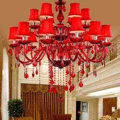 Large red crystal multi-tier chandelier with fabric shades and cascading crystals, in a grand interior setting.