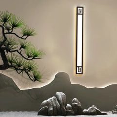 A single black geometric LED wall sconce mounted on a neutral wall, set against a backdrop of stylized rocks and a pine tree.