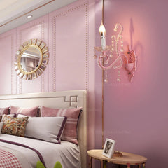 Pink wall sconce with crystal embellishments mounted on a pink paneled wall next to a bed