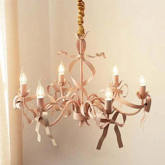 Close-up of a pink chandelier with candle-style bulbs and intricate ribbon detailing.
