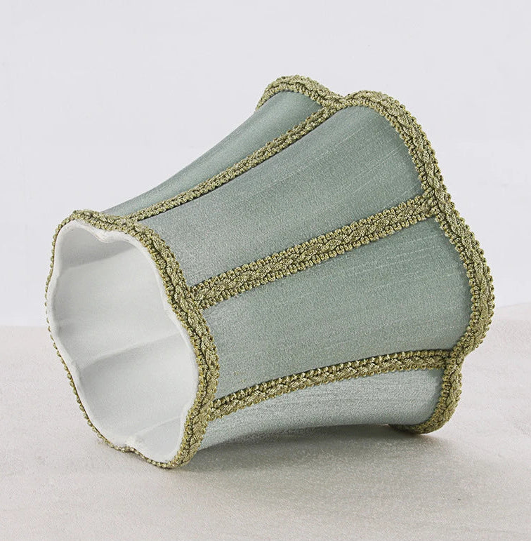 Close-up of a sky blue fabric lampshade with a scalloped top and bottom edge, trimmed with gold braided trim.