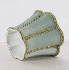 Close-up of a sky blue fabric lampshade with a scalloped top and bottom edge, trimmed with gold braided trim.