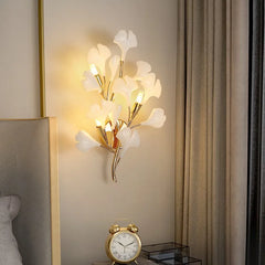 A gold ginkgo leaf wall sconce mounted on a wall above a nightstand, illuminating the bedside area.