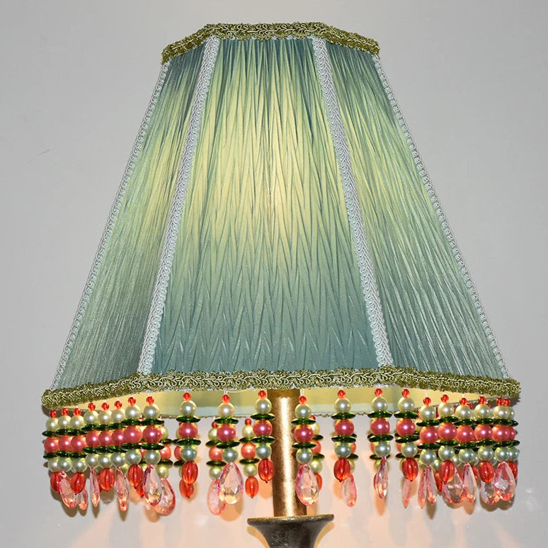Close-up of a light green pleated fabric empire lampshade adorned with beaded tassels in pink, green, and pearl colors.