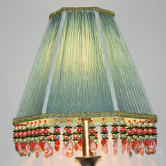 Close-up of a light green pleated fabric empire lampshade adorned with beaded tassels in pink, green, and pearl colors.