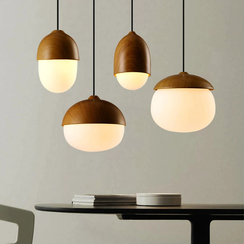 A grouping of four modern pendant lights with wood-textured tops and frosted glass diffusers, illuminated and hanging above a table.