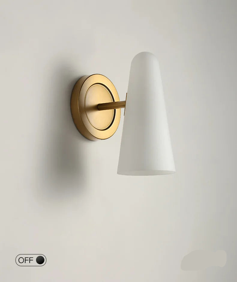 Wall-mounted light fixture with white shade and gold base on a plain background