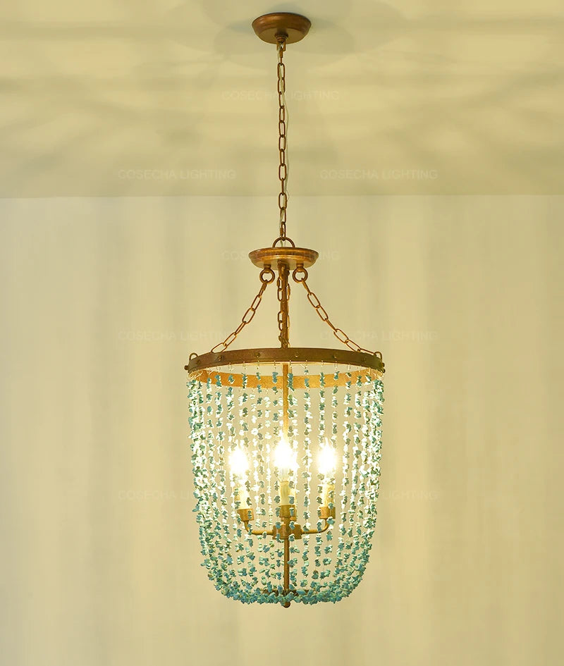 Turquoise stone bead chandelier with a distressed gold frame hanging from a chain against a light-colored ceiling.