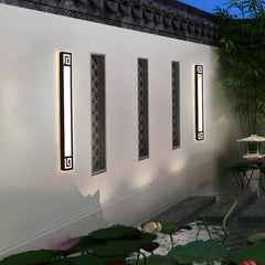 A black geometric LED wall sconce mounted on a white wall next to a tranquil pond with lotus flowers.