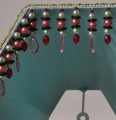Detail view of the beaded tassels hanging from the bottom edge of a green pleated fabric lampshade.