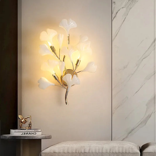 Close-up of a gold ginkgo leaf wall sconce, showcasing the delicate white leaf-shaped diffusers and gold stem.