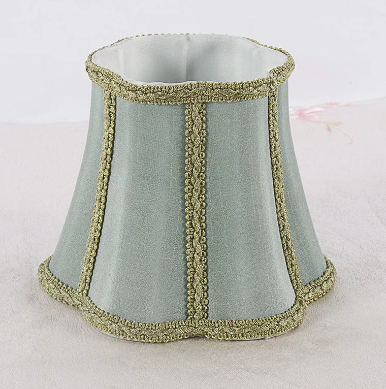 Front view of a sky blue fabric lampshade with a flared bell shape and gold braided trim along vertical seams.
