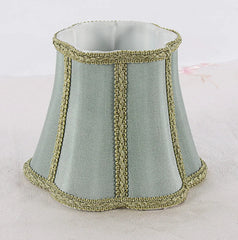 Front view of a sky blue fabric lampshade with a flared bell shape and gold braided trim along vertical seams.
