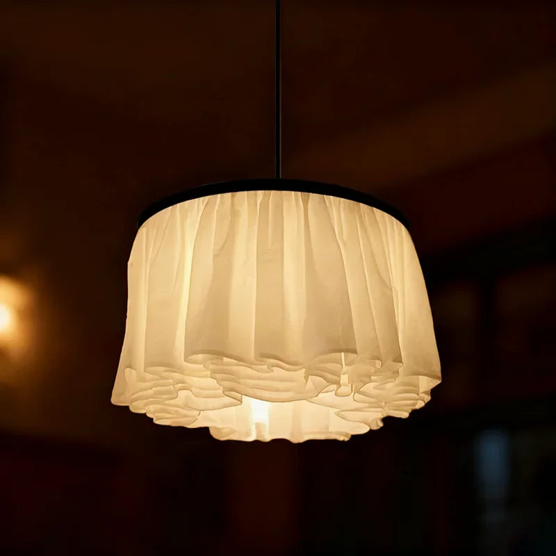 Close-up of a white fabric ruffled pendant light with a warm glow, hanging from a dark ceiling.