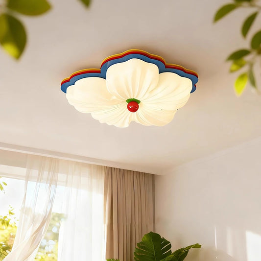 White flower-shaped flush mount ceiling light with multicolor accents, illuminated in a room with curtains and plants.