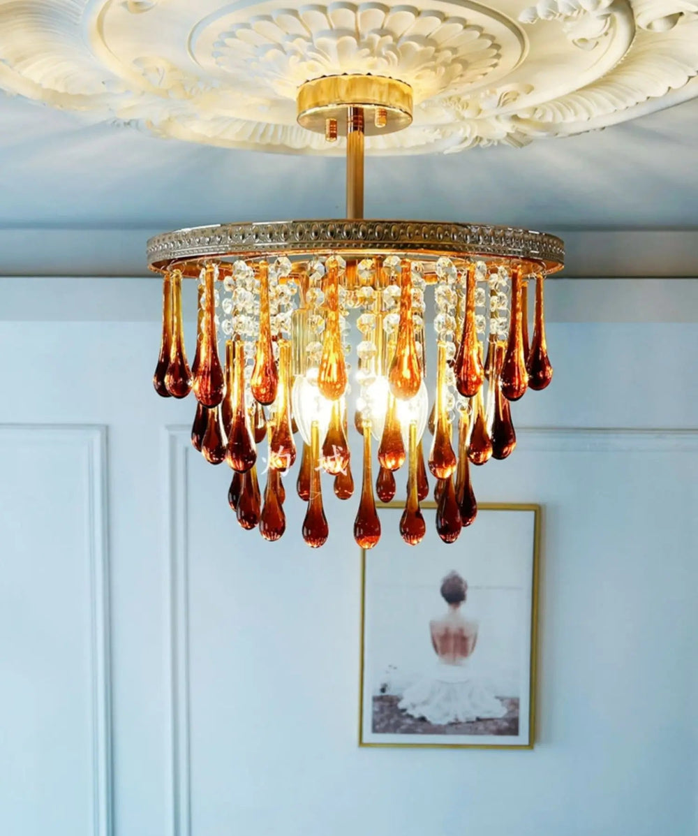 Chandelier with amber glass droplets in a room with light blue walls and a framed picture.