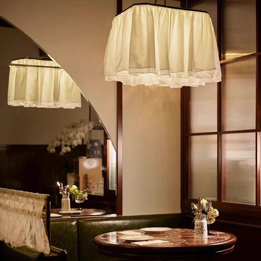 A white fabric ruffled pendant light hanging above a marble-top table in a restaurant setting, reflected in a mirror.