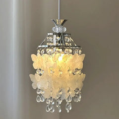 Close-up of a chrome pendant light with white butterfly-shaped shell accents and clear teardrop crystals.