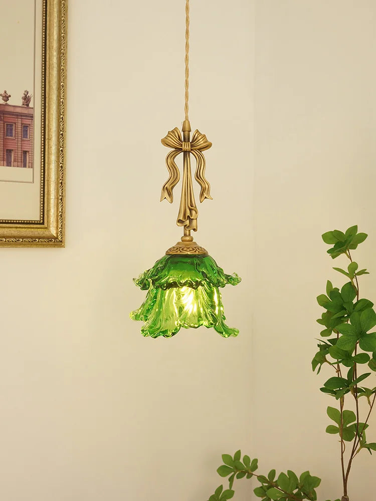 Green glass pendant light with gold fixture on a neutral wall.