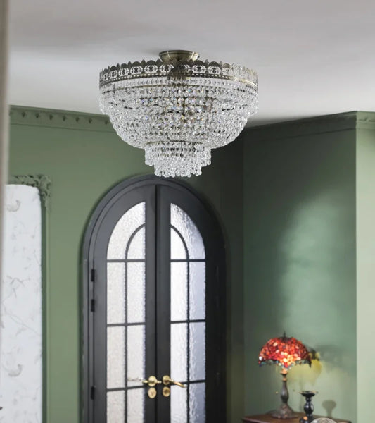Tiered crystal waterfall chandelier with polished chrome frame mounted on a ceiling in a room with green walls and a dark arched doorway.