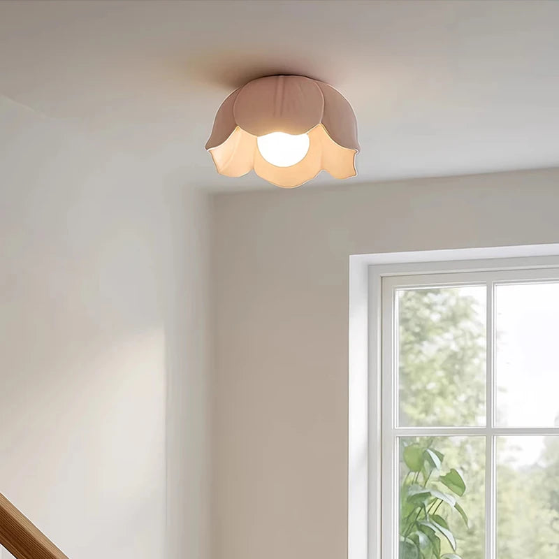 A pink ceramic flower-shaped semi-flush ceiling light installed in a hallway near a window and wooden banister.