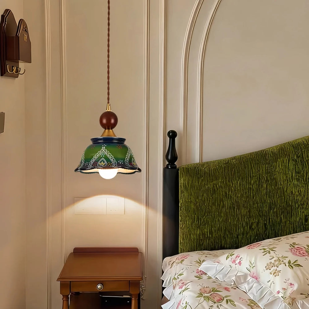 Green ceramic bell pendant light with hand-painted floral design hanging above a bedside table in a bedroom.