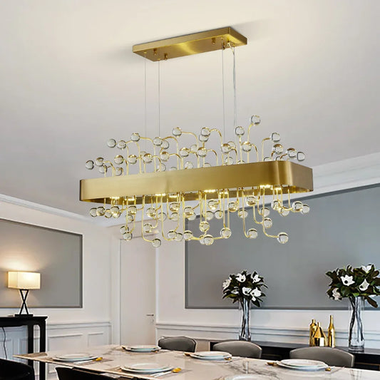 A rectangular gold chandelier with clear crystal accents hanging over a dining table.