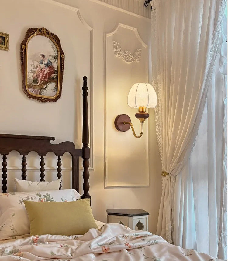 Bedroom with wooden bed, decorative pillows, wall sconce, and framed artwork.
