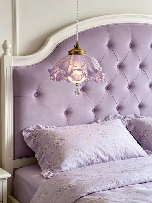 Purple floral lampshade with crystal accents hanging in front of a tufted purple headboard.